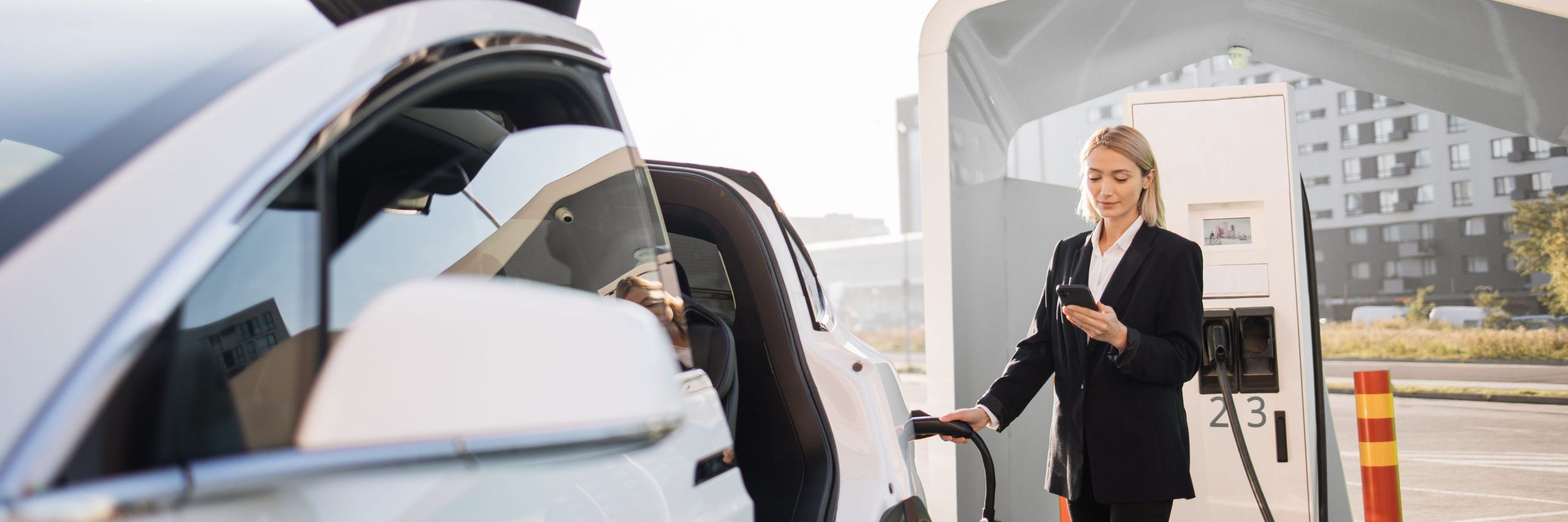 woman using smartphone and charging car outdoors