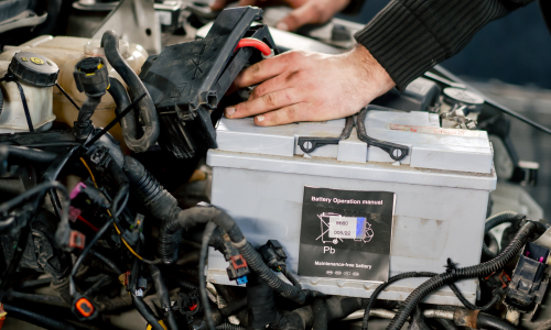 A mechanic's hands are shown carefully placing a new car battery into the engine bay.