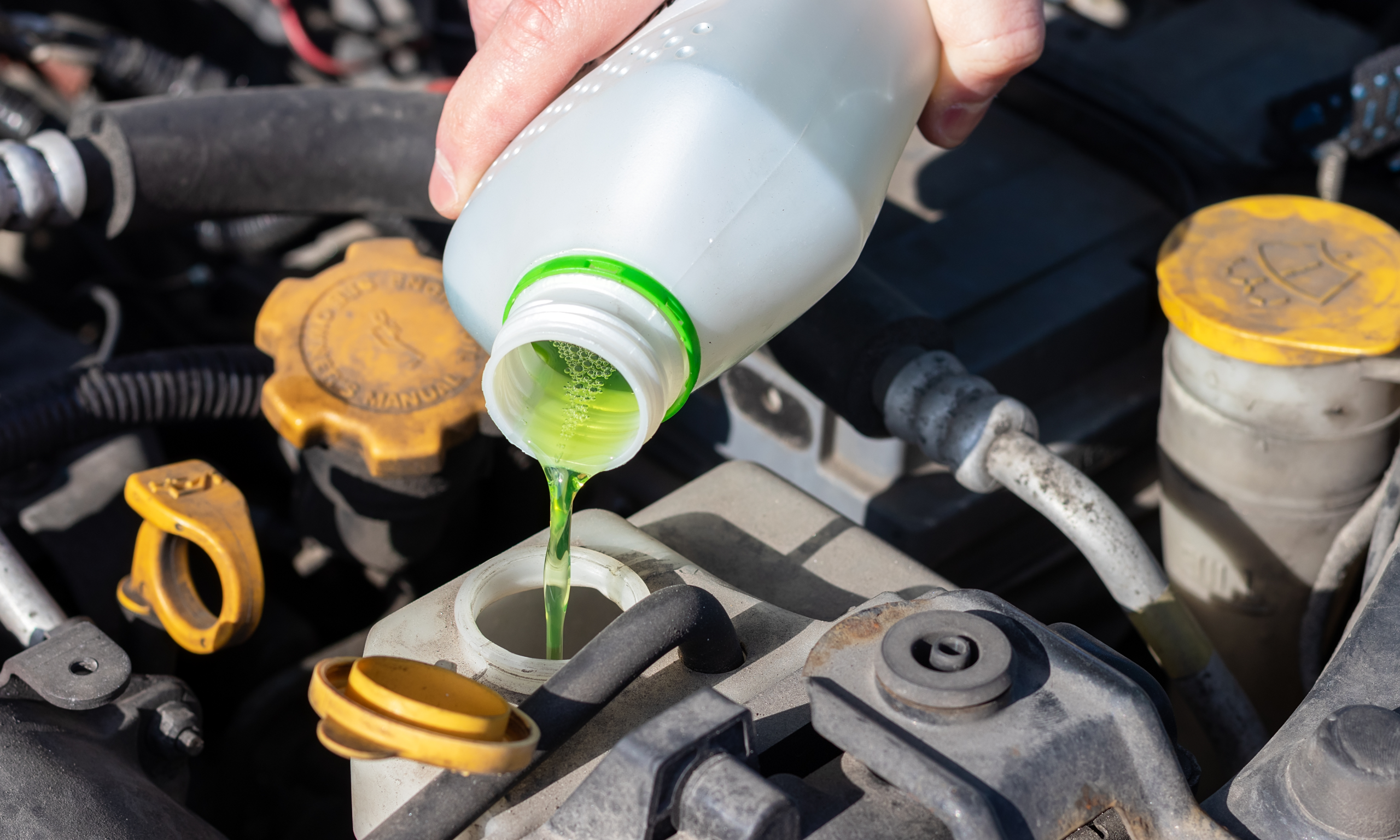 Green engine coolant being poured into a car’s reservoir, routine maintenance often done after a cambelt replacement.