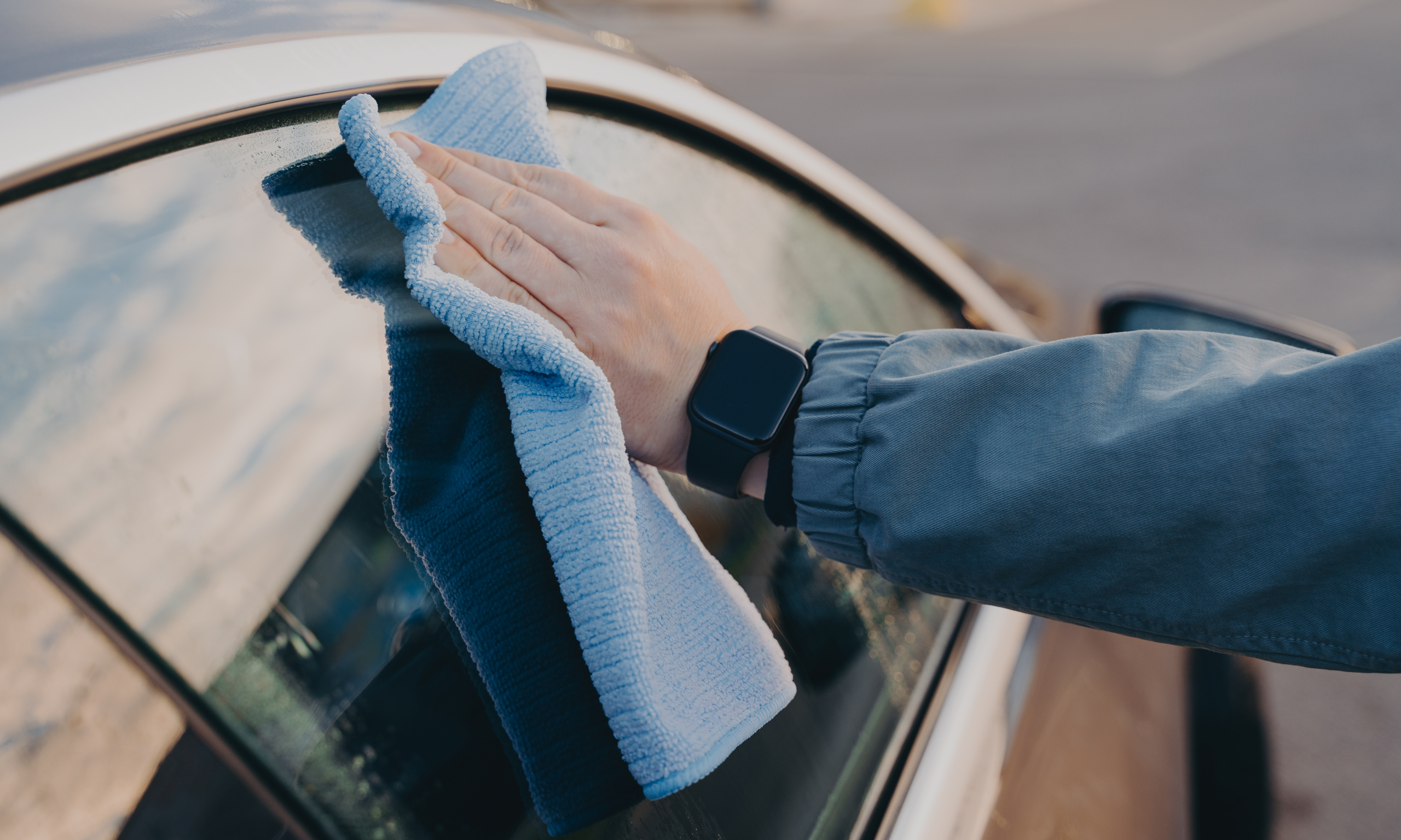 A person is cleaning a car window with a microfiber cloth after a car window repair at Acton Service Centre. The reflection on the glass and careful wiping show attention to detail in the repair process.