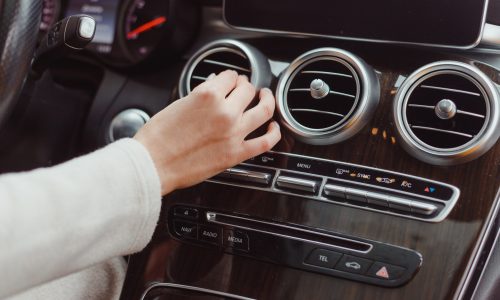 A woman's hand adjusting the controls of a car's air conditioning system, possibly to address an air con smell.