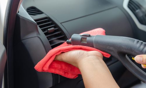 A person using a cleaning tool with a red cloth to clean a car's air con vent, suggesting a solution for air con smell.