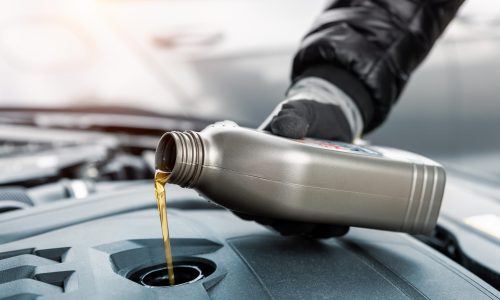 Close-up of a mechanic pouring fresh engine oil into Nissan car engine.