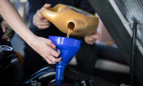 Technician adding fresh motor oil through a blue funnel during vehicle maintenance.