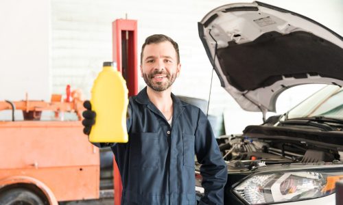 Smiling car mechanic holding a yellow motor oil container in an auto repair shop